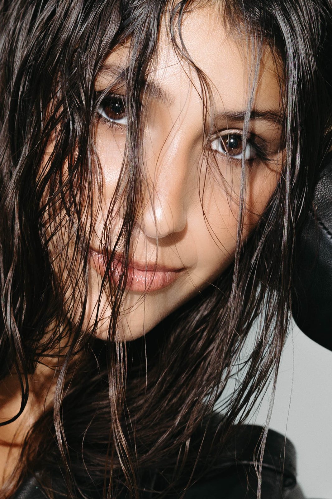 Close-up editorial portrait, wet dark hair across the face