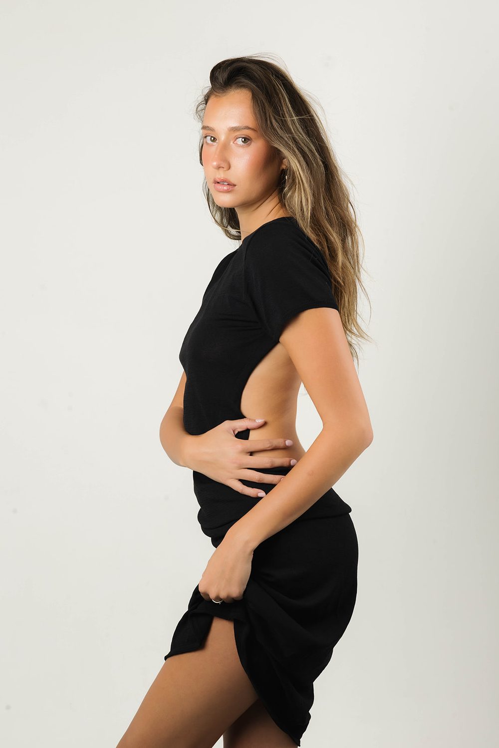 Model in profile glancing back over her shoulder in a black backless dress