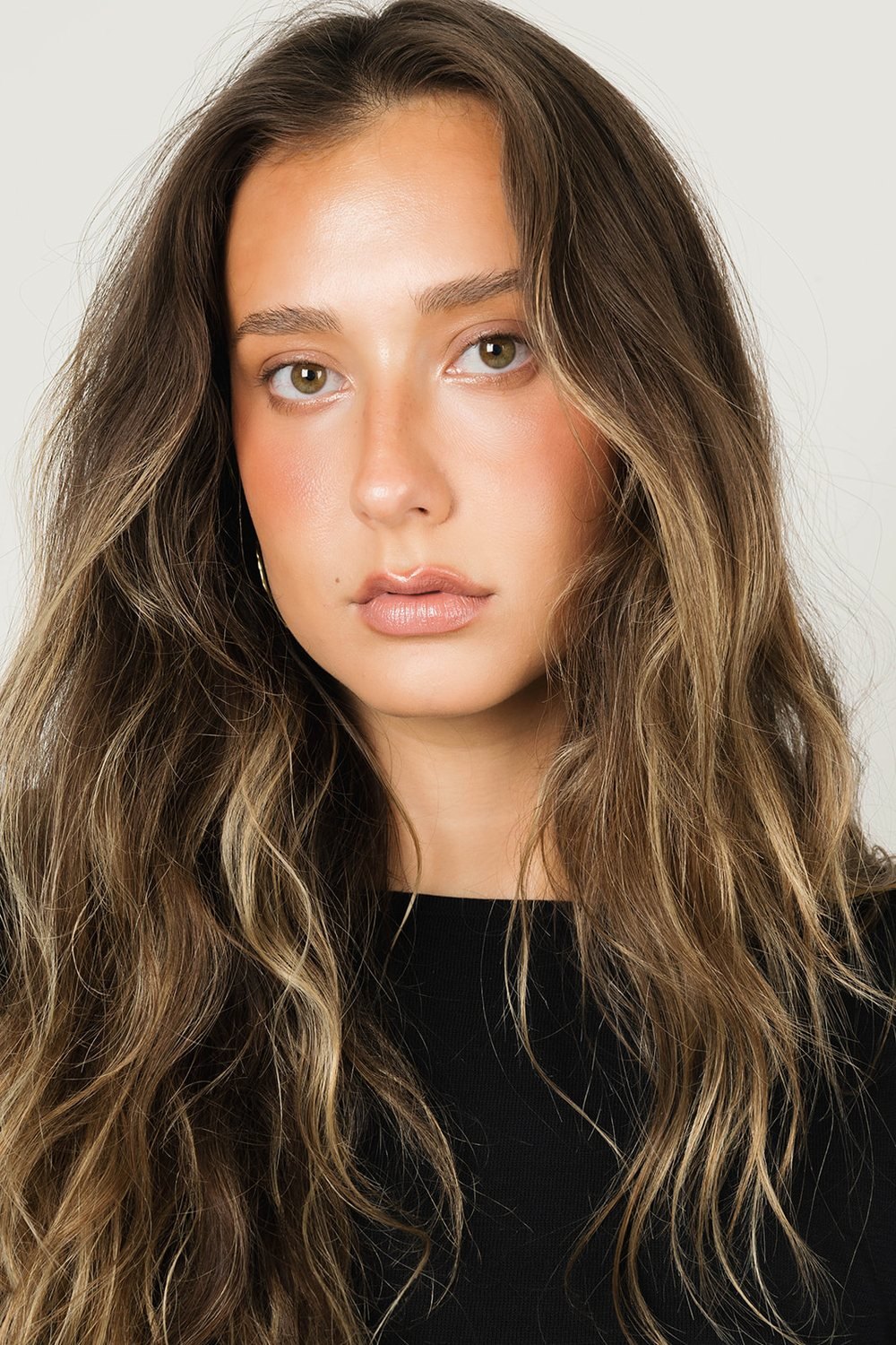 Close-up portrait of a model with long, wavy hair against a gray wall